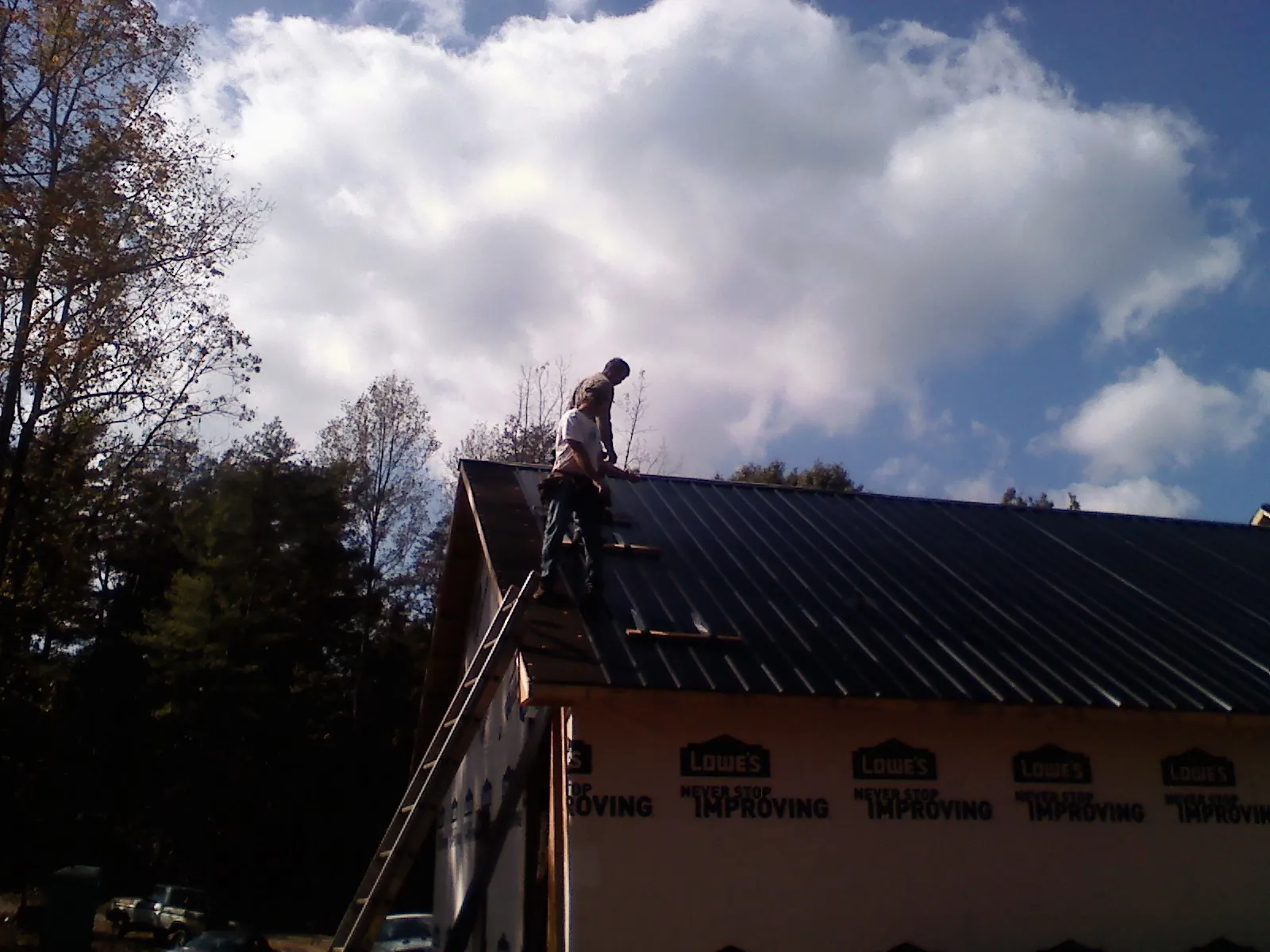 Roofer fastening dark metal panels high against a cloudy sky, from a Roof Inspection job in Alamo